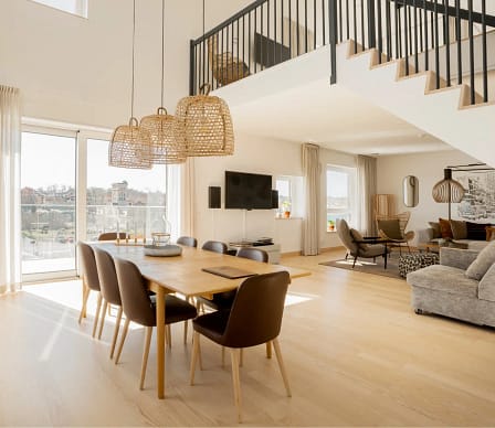 Rymligt vardagsrum och matplats i modern hotellsvit med stora fönster, balkong, skandinavisk inredning och ljusa trägolv.