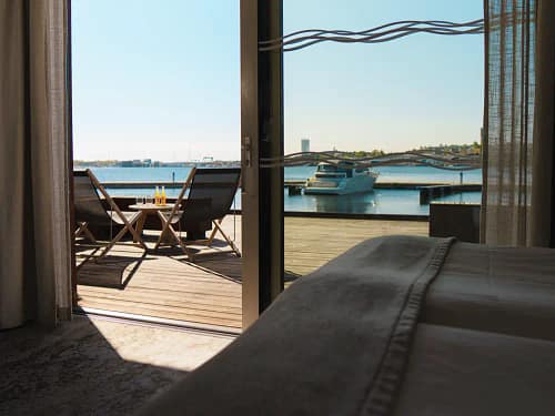 Hotellrum med terrass med utsikt över vatten och en brygga med båtar på Slottsholmens flytande hotell.